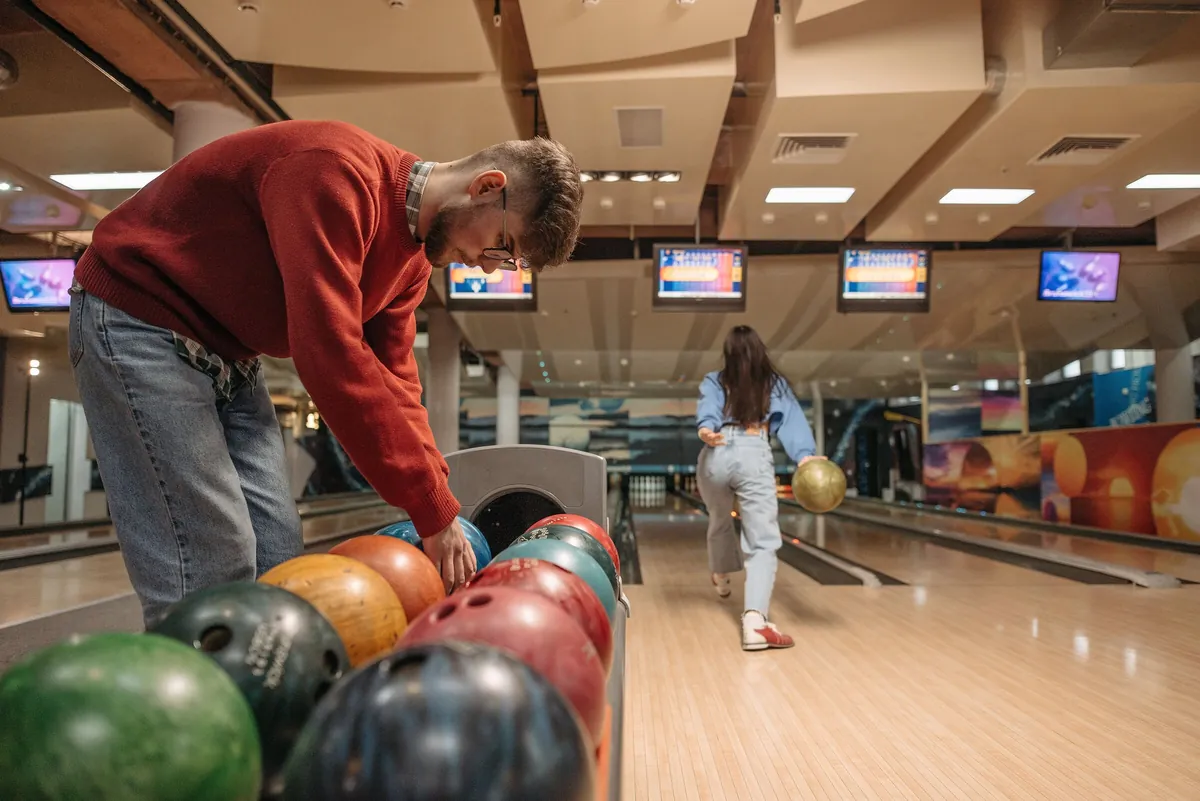 Joueur choisissant une boule de bowling sur un râtelier de boules colorées, piste en arrière-plan