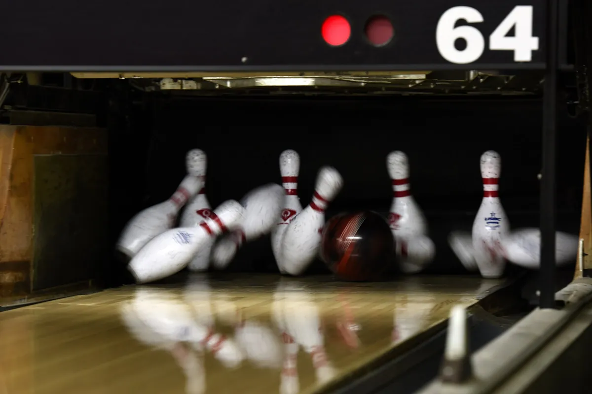 Boule de bowling percutant les quilles qui s'envolent au moment d'un strike sur la piste
