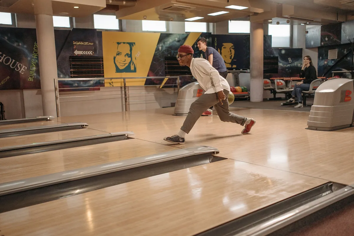 Jeune homme lançant sa boule de bowling sur la piste d'une salle de bowling moderne